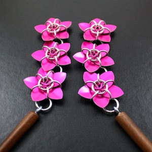 May include: A pair of pink flower-shaped earrings with silver accents. Each earring has five flowers connected together. The earrings are attached to wooden dowels.