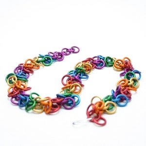 Może przedstawiać: Naszyjnik z łańcucha w kolorze tęczy wykonany z metalowych pierścieni. Łańcuch jest wykonany z naprzemiennych kolorów: czerwonego, pomarańczowego, żółtego, zielonego, niebieskiego, indygo i fioletowego.