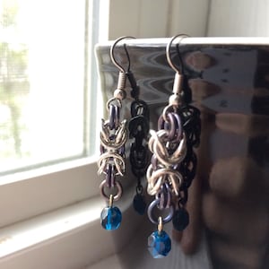 May include: A pair of silver and dark purple dangle earrings with blue crystal beads at the end.