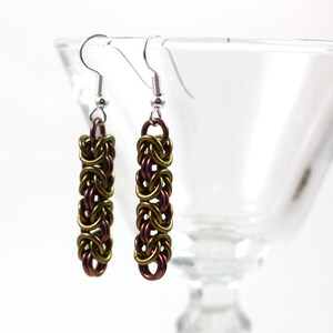 May include: A pair of long, dangling earrings with a woven chain design. The chain is made of metal with a gold and purple iridescent finish.