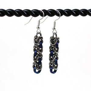 May include: A pair of silver and blue chainmail earrings with silver hooks. The earrings are made of small metal rings that are linked together to create a chainmail pattern.