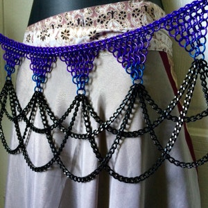 May include: A black chain belt with a purple and blue chainmail top. The chainmail top has a triangular shape with three points. The chainmail is made of small metal rings.
