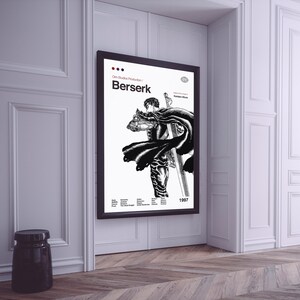 May include: A black and white poster with the title "Berserk" in red text. The poster features a black and white illustration of a character from the anime series Berserk. The poster is framed in black and hanging on a white wall.