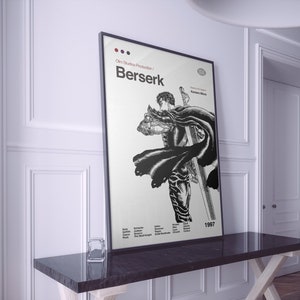 May include: A black and white poster with the title "Berserk" and the text "Olm Studios Production" in a white frame. The poster features a black and white illustration of a character from the anime series Berserk, holding a large sword. The poster also includes the year 1997.
