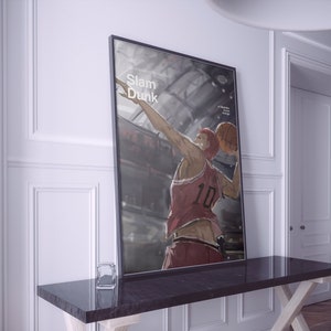 May include: A black framed poster with the text "Slam Dunk" in white. The poster features a basketball player in a red jersey with the number 10 on it, holding a basketball and jumping in the air.