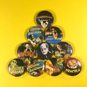 May include: A collection of round pinback buttons featuring classic horror movie imagery. The buttons display images and titles from films like "Frankenstein," "Dracula," and "Creature from the Black Lagoon" against a yellow background.