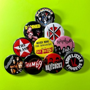 May include: A collection of ten circular pin-back buttons featuring punk rock band imagery and logos. The buttons display graphics for The Ramones, The Damned, Dead Kennedys, The Clash, Sex Pistols, New York Dolls, The Stooges, Sham 69, Buzzcocks, and Stiff Little Fingers with various text and band member portraits.