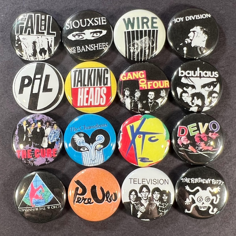 Puede incluir: Una colecci&oacute;n de diecis&eacute;is botones redondos con nombres y logotipos de bandas. Los botones muestran texto y gr&aacute;ficos en negro, blanco, rojo, amarillo y azul. Las bandas incluyen The Cure, Pere Ubu y Television.