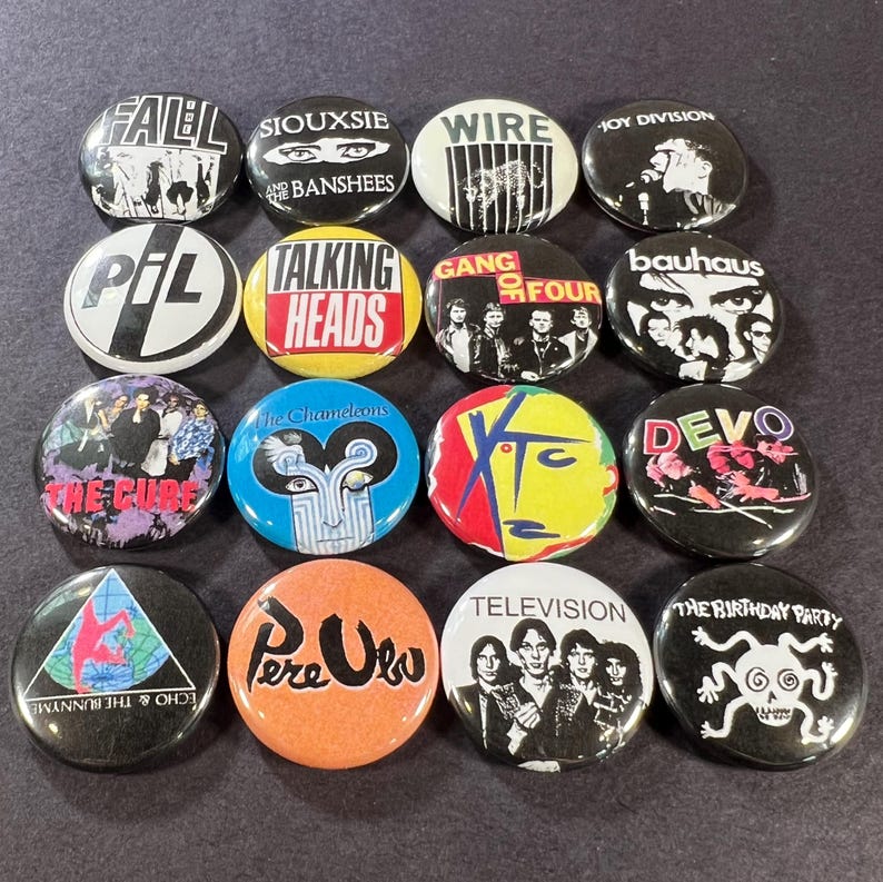 Puede incluir: Una colecci&oacute;n de diecis&eacute;is botones redondos con nombres y logotipos de bandas. Los botones muestran varios colores y dise&ntilde;os, incluyendo texto y gr&aacute;ficos. Las bandas incluyen The Fall, Siouxsie and the Banshees, Wire, Joy Division, PIL, Talking Heads, Gang of Four y Bauhaus.