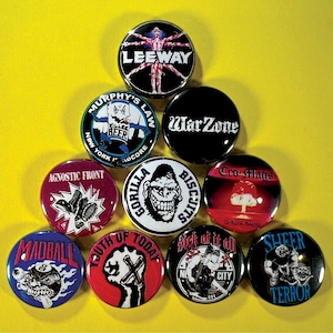 May include: A collection of round, black, and colorful pinback buttons with various band logos and text. The buttons feature designs like "LEEWAY," "WarZone," and "Gorilla Biscuits," set against a yellow background.