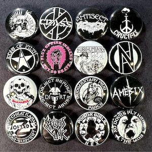 Pode incluir: Uma coleção de dezasseis botões de punk rock em preto e branco. Cada botão apresenta nomes de bandas e gráficos, incluindo caveiras, logotipos e texto. Os botões são redondos e têm um acabamento brilhante.