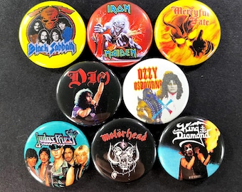 May include: A collection of eight round metal pinback buttons featuring various rock band logos and album art. Bands include Black Sabbath, Iron Maiden, Dio, Ozzy Osbourne, Judas Priest, Motörhead, and King Diamond. The buttons have a glossy finish.