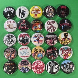 May include: A selection of 25 circular pin badges showcasing iconic rock bands and musicians. The badges feature band logos, album artwork, and artist names, such as Led Zeppelin, The Beatles, and The Rolling Stones.