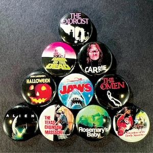 May include: A selection of ten circular pin badges showcasing classic horror film titles and visuals. Films represented include "The Exorcist," "Dawn of the Dead," "Carrie," "Halloween," "Jaws," "The Omen," "Alien," "The Texas Chainsaw Massacre," "Rosemary's Baby," and "Invasion of the Body Snatchers."