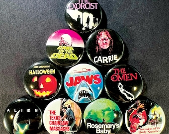 May include: A collection of ten round pinback buttons featuring iconic horror movie titles and imagery. Titles include "The Exorcist," "Dawn of the Dead," "Carrie," "Halloween," "Jaws," "The Omen," "Alien," "The Texas Chainsaw Massacre," "Rosemary's Baby," and "Invasion of the Body Snatchers."