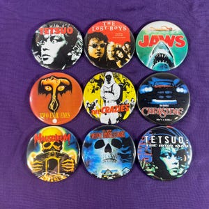 May include: Nine circular button badges with film-themed designs. The badges display graphics and text from movies including "Tetsuo," "The Lost Boys," "Jaws," "Two Evil Eyes," "The Crazies," "Christine," "Mausoleum," "People Under the Stairs," and "Tetsuo: The Iron Man."