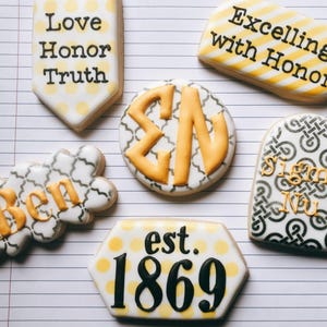 May include: Assortment of decorated cookies with various designs and text. One cookie reads "Love Honor Truth", another "Excelling with Honor". Other cookies feature "Ben", "Sigma Nu", and "est. 1869". The cookies have white, yellow, and black icing.