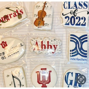 May include: Assortment of decorated sugar cookies in clear packaging. Designs include a violin, musical notes, the word "Congrats", "Class of 2022", the name "Abby", and the words "Jacobs School of Music" and "Interlochen".