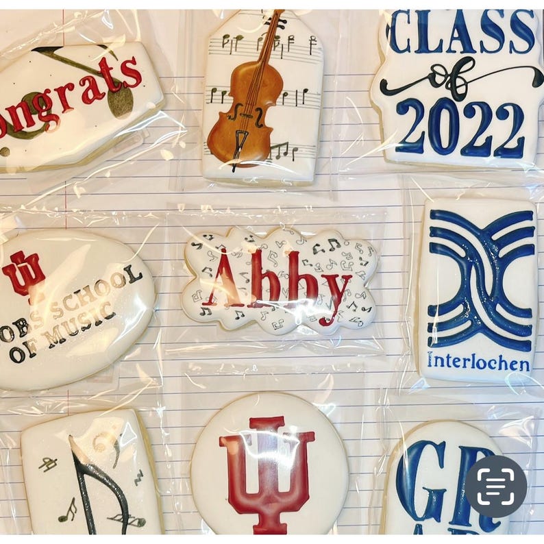 May include: Assortment of decorated sugar cookies in clear packaging. Designs include a violin, musical notes, the word "Congrats", "Class of 2022", the name "Abby", and the words "Jacobs School of Music" and "Interlochen".