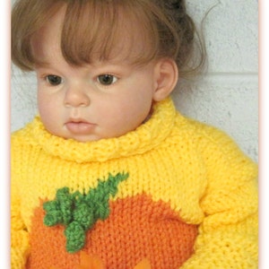 K&ouml;nnte beinhalten: Ein gelber und orangefarbener Strickpullover mit einem gr&uuml;nen Blattdesign. Der Pullover ist ein K&uuml;rbis-Kost&uuml;m f&uuml;r ein Baby.