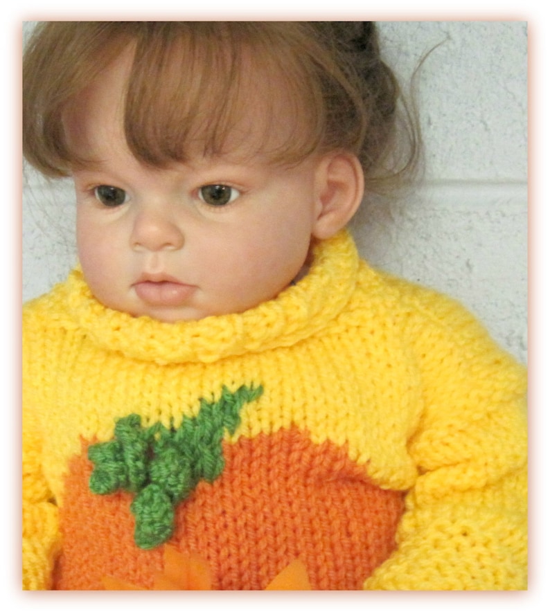 K&ouml;nnte beinhalten: Ein gelber und orangefarbener Strickpullover mit einem gr&uuml;nen Blattdesign. Der Pullover ist ein K&uuml;rbis-Kost&uuml;m f&uuml;r ein Baby.