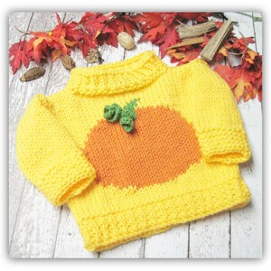 K&ouml;nnte beinhalten: Ein gelber Strickpullover mit einem orangefarbenen K&uuml;rbisdesign und gr&uuml;nen Bl&auml;ttern. Der Pullover hat einen Rundhalsausschnitt und lange &Auml;rmel.