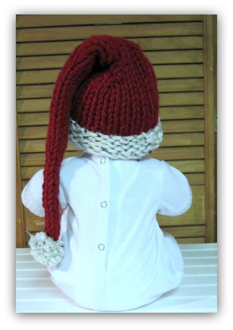 May include: A red knitted hat with a long, white pom-pom on the end. The hat has a white brim and is worn by a baby.