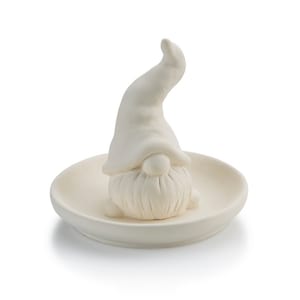 May include: White ceramic gnome ring holder with a raised hat and beard. The gnome is sitting on a small white ceramic dish.