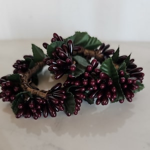 May include: Two burgundy grapevine napkin rings with green leaves. The rings are made of artificial grapes and leaves.