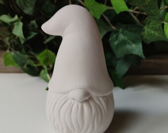 May include: A white ceramic gnome figurine with a rounded hat and a detailed beard. The gnome is standing on a white surface.