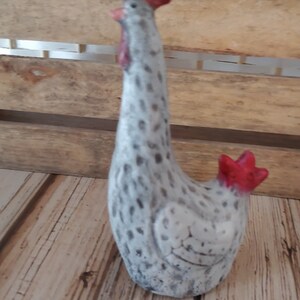 Puede incluir: Una figurita de gallo de cer&aacute;mica blanca con manchas negras y una cresta y barbillas rojas. El gallo est&aacute; de pie sobre una superficie de madera.