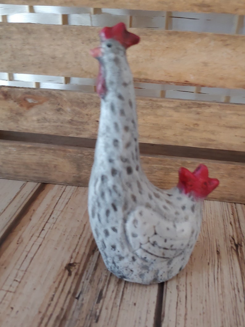 Puede incluir: Una figurita de gallo de cer&aacute;mica blanca con manchas negras y una cresta y barbillas rojas. El gallo est&aacute; de pie sobre una superficie de madera.