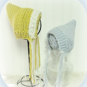 May include: Two knitted baby bonnets, one yellow with white trim and one light blue, displayed on stands.