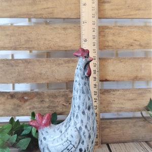 Puede incluir: Una figurita de cer&aacute;mica blanca de pollo con manchas negras y detalles rojos. El pollo est&aacute; de pie con la cabeza inclinada hacia un lado. La figurita mide aproximadamente 18 cm de alto.