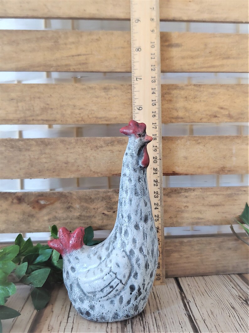Puede incluir: Una figurita de cer&aacute;mica blanca de pollo con manchas negras y detalles rojos. El pollo est&aacute; de pie con la cabeza inclinada hacia un lado. La figurita mide aproximadamente 18 cm de alto.