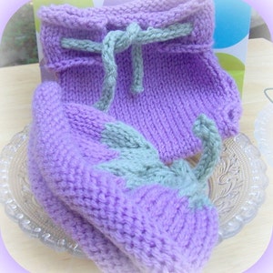 May include: A set of lavender knitted baby booties with a green knitted trim. The booties are tied with a green ribbon.