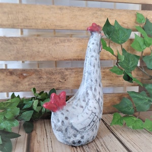 Puede incluir: Una figurita de pollo de cer&aacute;mica blanca con manchas negras y detalles rojos. El pollo est&aacute; de pie con la cabeza echada hacia atr&aacute;s.