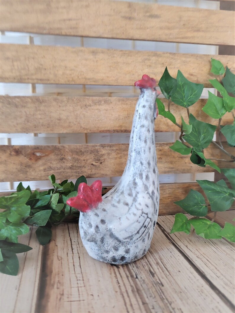 Puede incluir: Una figurita de pollo de cer&aacute;mica blanca con manchas negras y detalles rojos. El pollo est&aacute; de pie con la cabeza echada hacia atr&aacute;s.