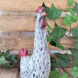 Puede incluir: Una figurita de cer&aacute;mica blanca de pollo con manchas negras y detalles rojos. El pollo est&aacute; de pie con la cabeza inclinada hacia un lado.
