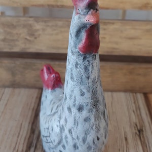 Puede incluir: Una figurita de cer&aacute;mica blanca de pollo con manchas negras y una cresta y barbillas rojas. El pollo est&aacute; de pie con la cabeza inclinada hacia un lado.