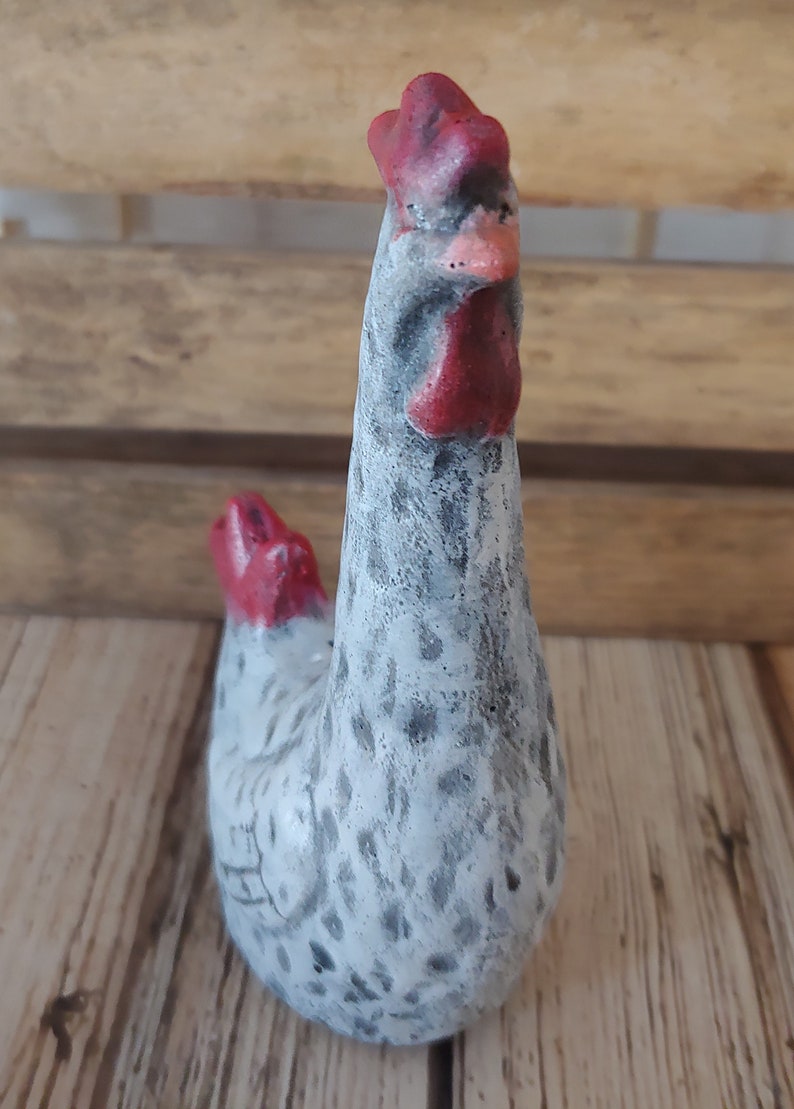Puede incluir: Una figurita de cer&aacute;mica blanca de pollo con manchas negras y una cresta y barbillas rojas. El pollo est&aacute; de pie con la cabeza inclinada hacia un lado.