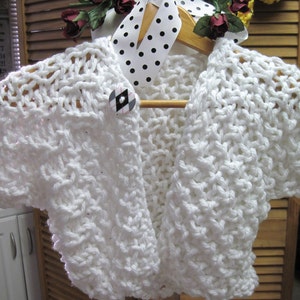 May include: White crocheted shrug with a black and white checkered button.