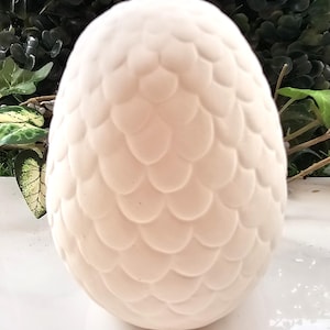 May include: White ceramic dragon egg with a textured, scaly surface. The egg is a blank canvas for painting and decorating.