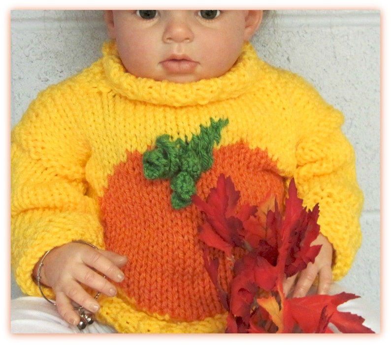 K&ouml;nnte beinhalten: Ein gelber Strickpullover mit einem orangefarbenen K&uuml;rbisdesign und gr&uuml;nen Bl&auml;ttern. Der Pullover hat einen Rollkragen und lange &Auml;rmel.