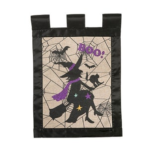 May include: A black and white Halloween garden flag with a silhouette of a witch flying on a broomstick with a cat. The witch is wearing a purple scarf and hat. The background is a beige fabric with a spiderweb pattern and the word "Boo!" in purple glitter.