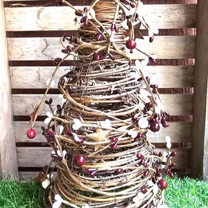 May include: A brown twig Christmas tree decorated with white and burgundy berries. The tree is sitting on a green artificial grass surface.