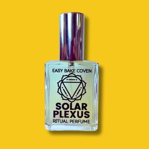 Può includere: Flacone di profumo trasparente con tappo argentato e liquido verde chiaro. L'etichetta riporta la scritta "EASY BAKE COVEN", un disegno geometrico nero e "SOLAR PLEXUS RITUAL PERFUME". Sfondo giallo brillante.