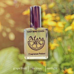 May include: A clear glass fragrance bottle with a silver cap. The label reads "EASY BAKE COVEN Ostara Fragrance Potion" with a grapefruit slice illustration. The background features yellow flowers and green foliage.