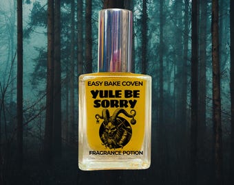 May include: A clear glass perfume bottle with a silver cap containing a yellow liquid. The label reads EASY BAKE COVEN, YULE BE SORRY, and FRAGRANCE POTION, featuring a black graphic illustration of a horned creature with a beard.