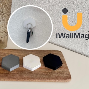 Könnte beinhalten: Ein Holztablett zeigt drei sechseckige magnetische Schlüsselhalter in Grau, Weiß und Schwarz. Ein weißer sechseckiger Schlüsselhalter ist an einer Wand montiert und hält Schlüssel. Das Bild enthält ein Glas, eine Vase und den Text "iWallMag".